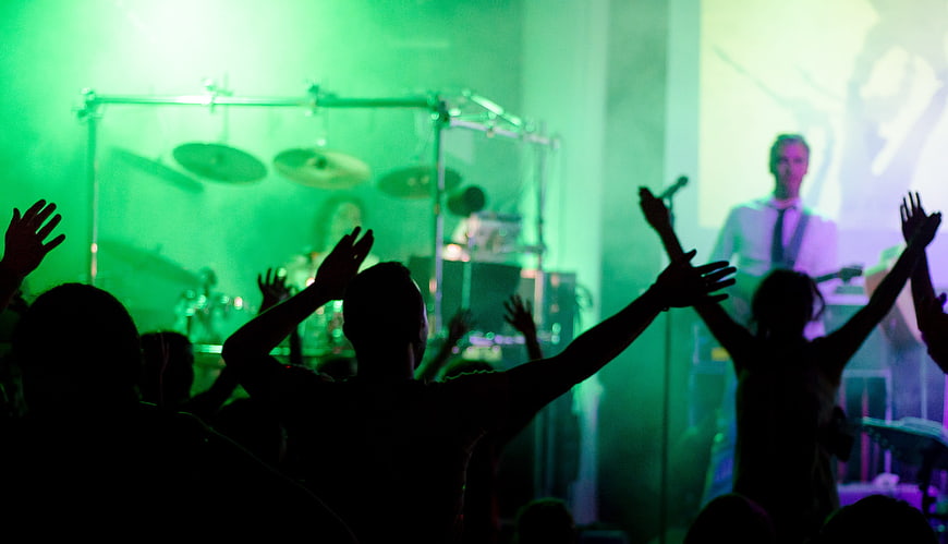 Silhouettes of crowd cheering at live concert with green stage lights