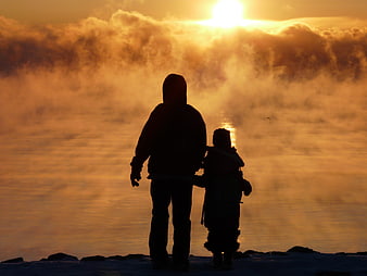 Silhouette of father and son watching sunrise over misty lake