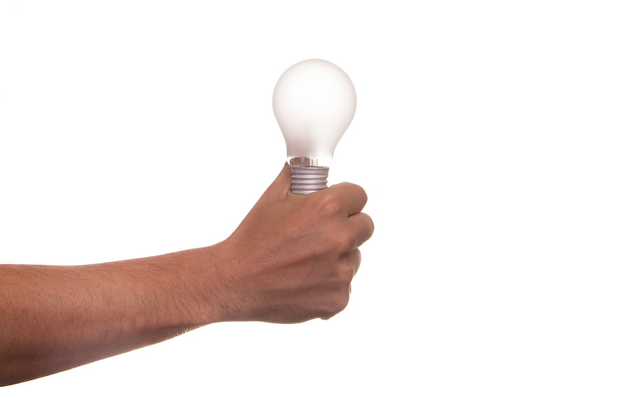 Hand holding glowing light bulb on white background