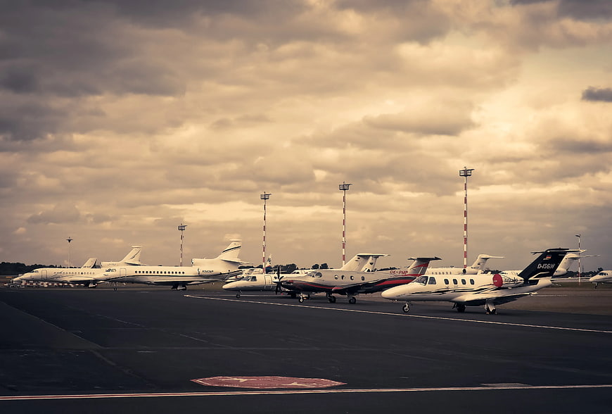 Private jets parked on airport tarmac under cloudy sky