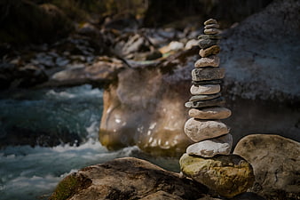 Stacked stones cairn by flowing river stream
