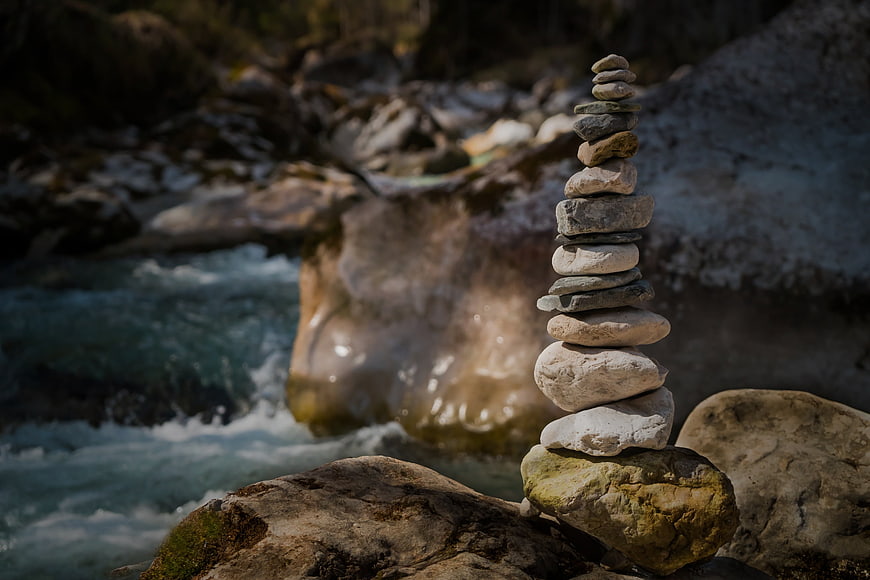 Stacked stones cairn by flowing river stream
