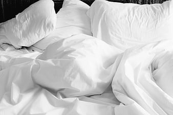 Unmade white bed with rumpled sheets and pillows
