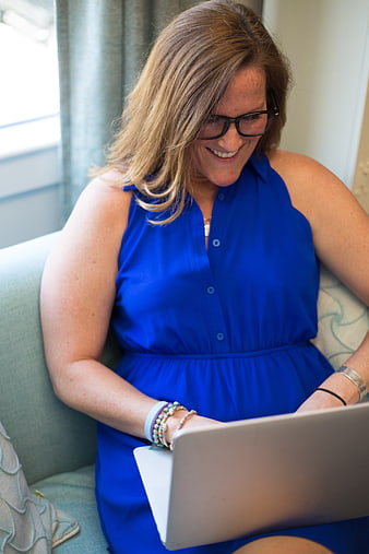 Smiling woman in blue dress using laptop on sofa