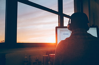 Man working on computer at desk with sunset view through window