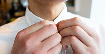 Close-up of man buttoning white shirt collar