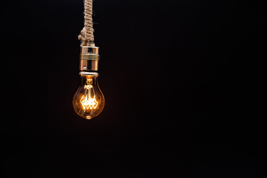 Vintage Edison Light Bulb Hanging On Rope Against Black Background