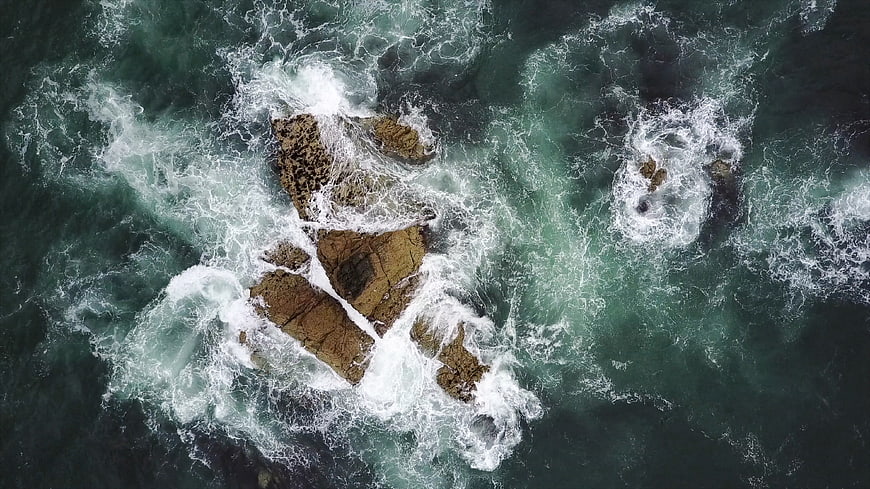 Aerial View of Turbulent Ocean Waves Crashing on Rocks