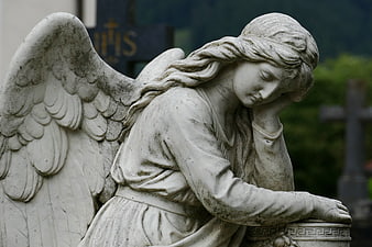 Mournful Angel Statue in Cemetery with Blurred Cross Background