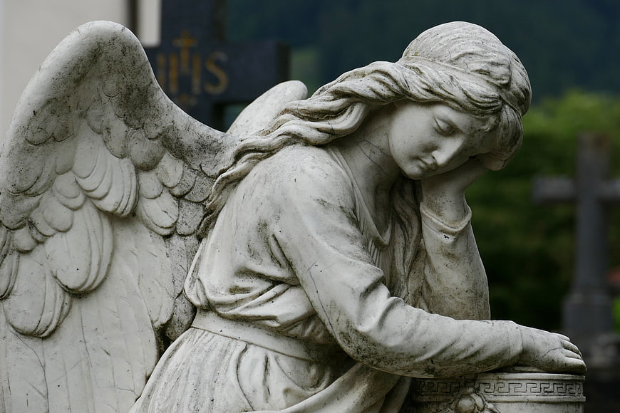 Mournful Angel Statue in Cemetery with Blurred Cross Background