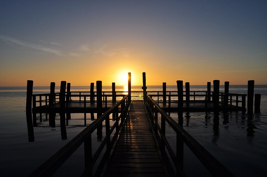 Silhouetted Wooden Dock at Golden Sunset Over Calm Ocean