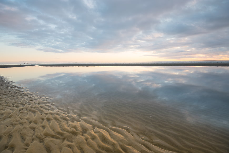 Serene beach landscape with rippled sand and sky reflection at sunset