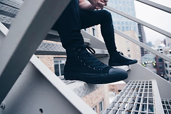 Man in Black Sneakers Sitting on Industrial Metal Stairs
