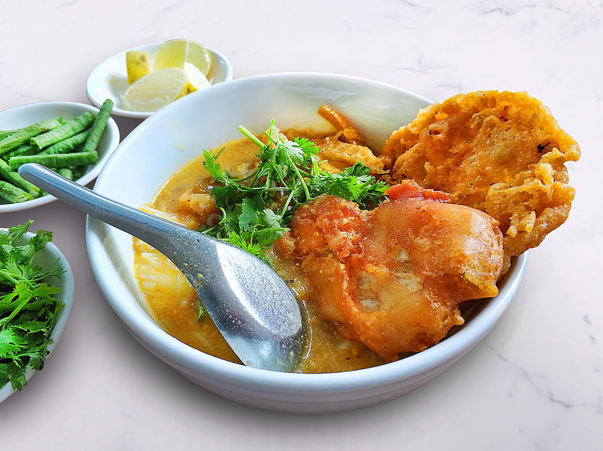 Traditional Burmese Mohinga Noodle Soup with Fried Fish and Garnishes