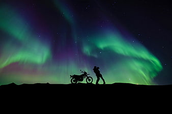 Silhouette of couple kissing with motorcycle under green aurora borealis night sky