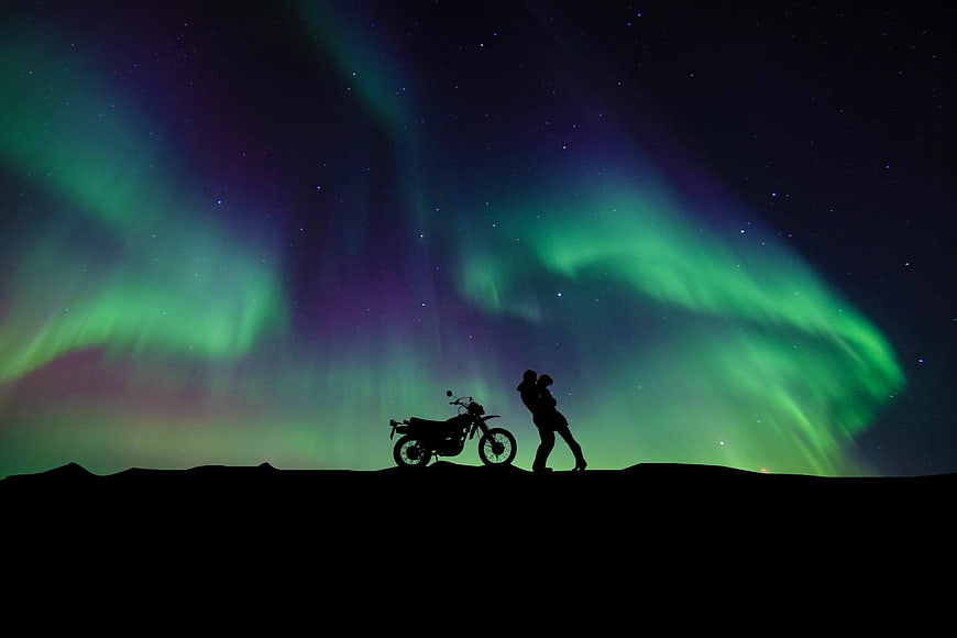 Silhouette of couple kissing with motorcycle under green aurora borealis night sky