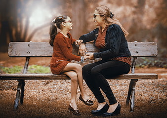 Mother and daughter sitting on park bench holding hands
