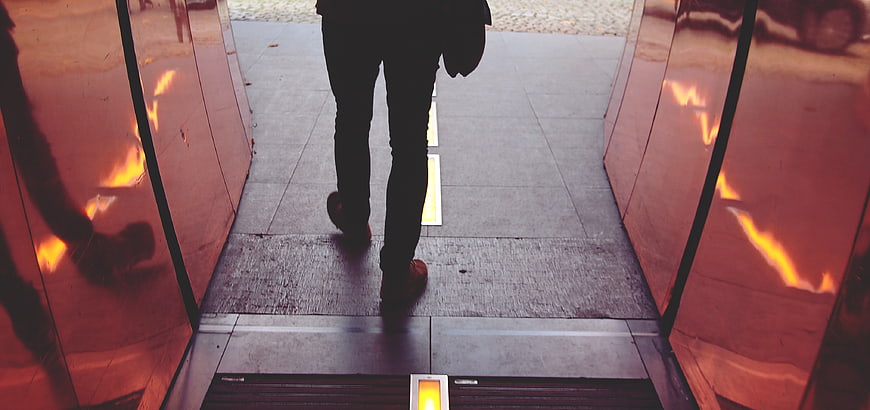 Man Walking Through Glass Doors with Orange Reflections