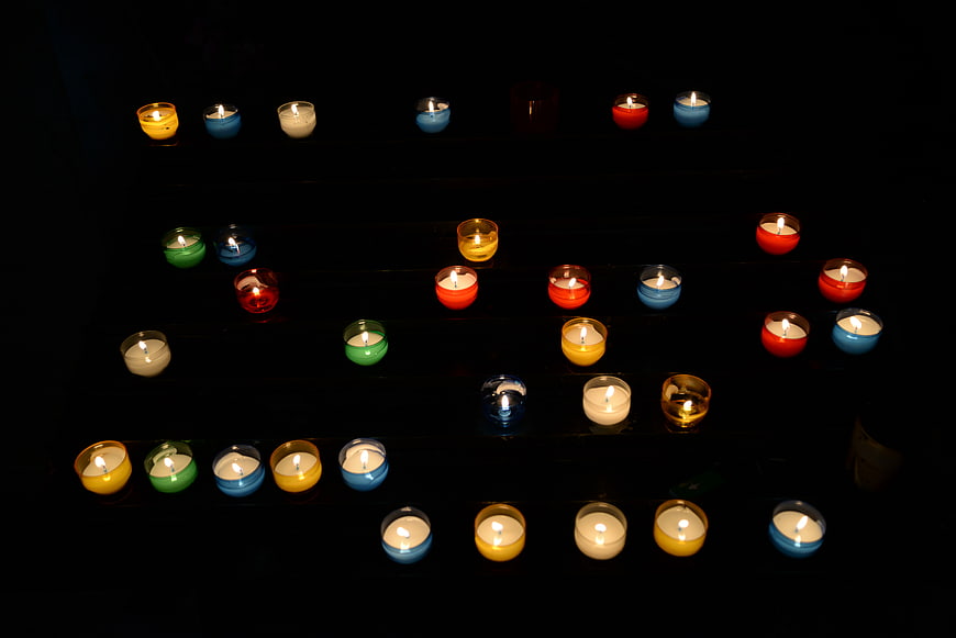 Colorful lit candles arranged in rows on dark background