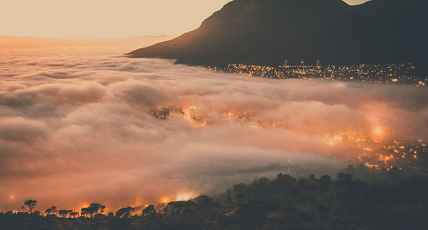 City lights glowing through thick fog in mountain valley at dusk