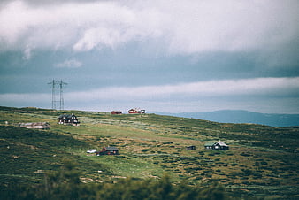 Remote cabins on a green hillside under cloudy sky