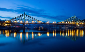 Illuminated Steel Truss Bridge At Dusk With Water Reflections