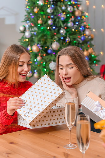 Two happy women opening Christmas gifts by a tree