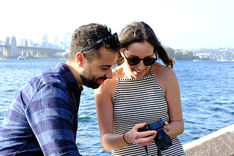 Happy couple reviewing photos on camera by the water