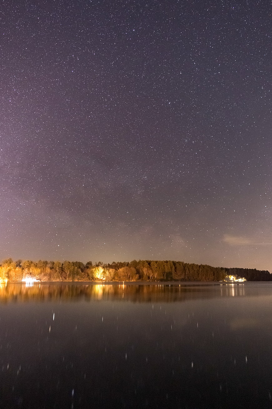 Starry Night Sky Over Lake With Forest Reflection