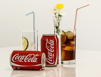 Coca-Cola cans and glasses with ice and lime on white background