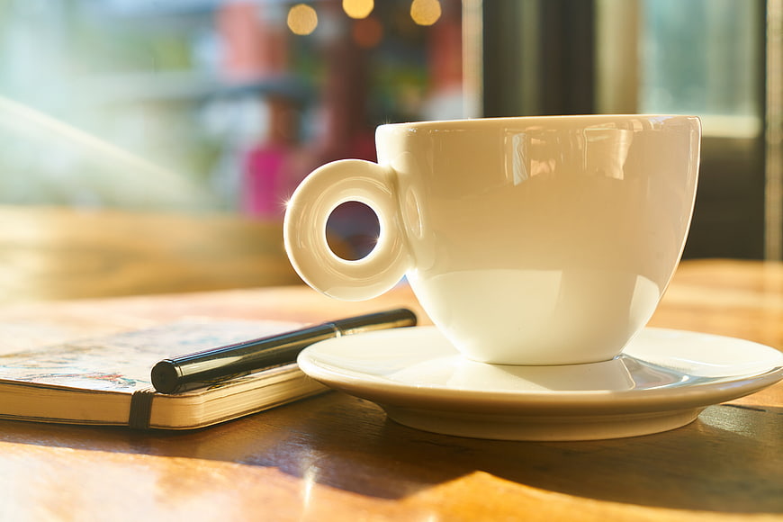 White Coffee Cup on Wooden Table with Notebook and Pen