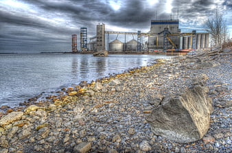 Industrial plant on rocky riverbank under dramatic cloudy sky