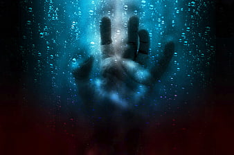 Silhouette of hand pressing against wet glass with water droplets