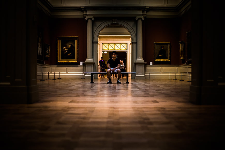 Man sitting alone on bench in grand museum gallery