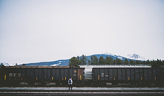 Man Standing by Freight Train Tracks with Snowy Mountains