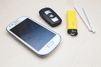 White smartphone, car key, lighter, and cigarettes on table
