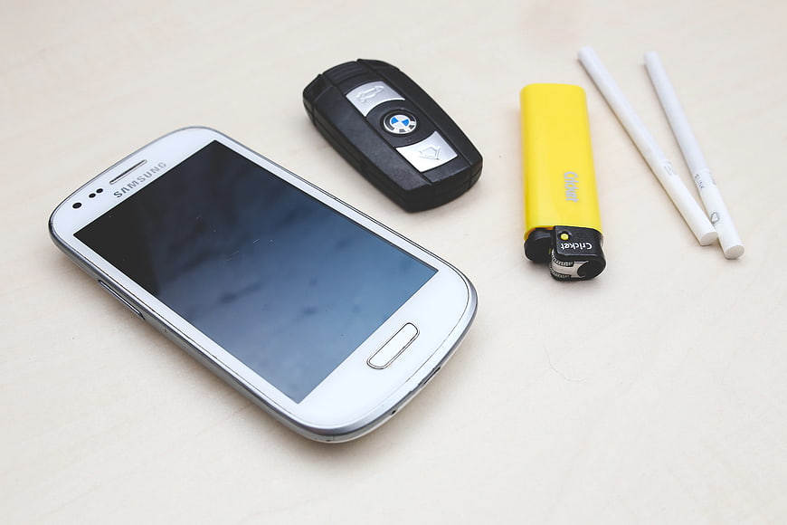 White smartphone, car key, lighter, and cigarettes on table