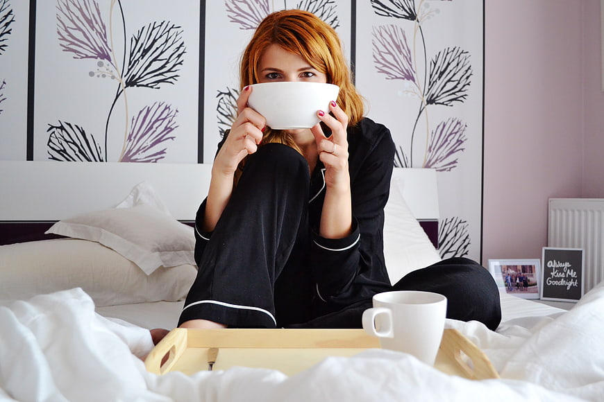 Woman in black pajamas eating breakfast in bed with coffee