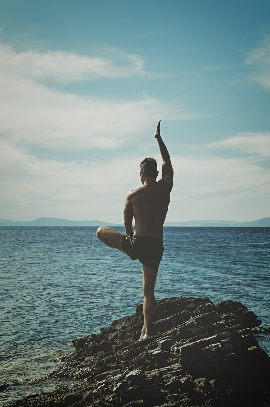 Man doing yoga on rocky shore by the ocean