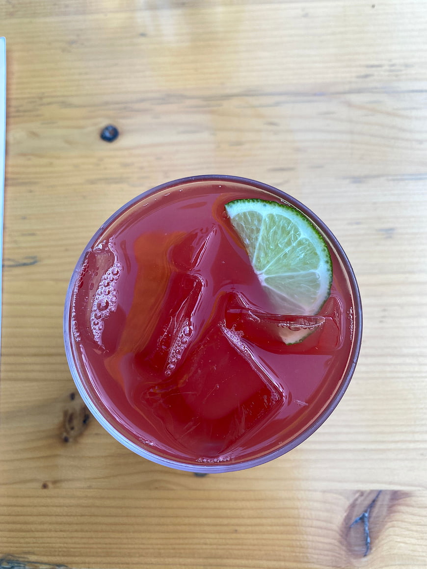 Top View of Red Cocktail with Lime and Ice on Wood