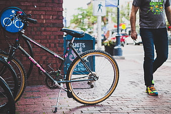 Black bicycle parked on brick sidewalk with pedestrian walking by