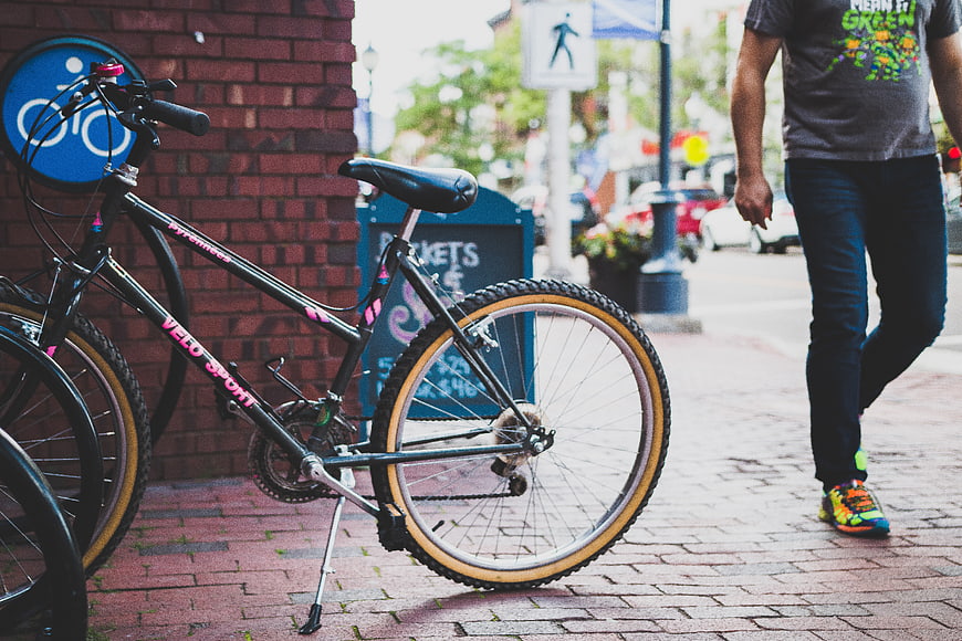 Black bicycle parked on brick sidewalk with pedestrian walking by