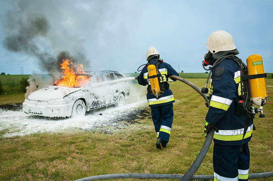 Firefighters extinguishing a burning car with foam