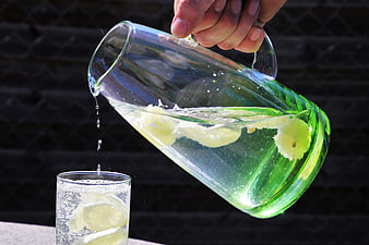 Hand pouring lemon water from glass pitcher into glass