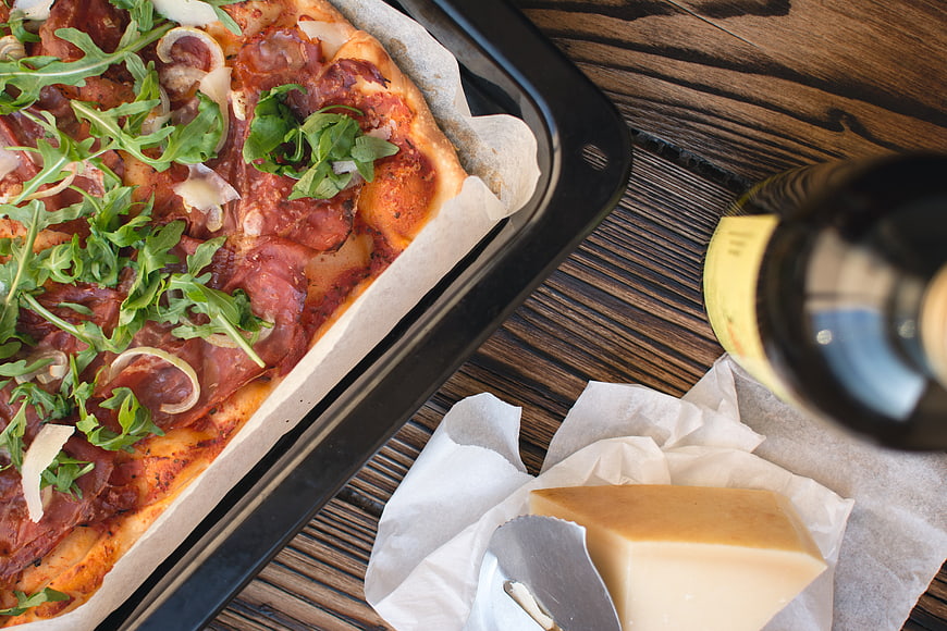 Homemade pizza with arugula, cheese, and wine on wooden table