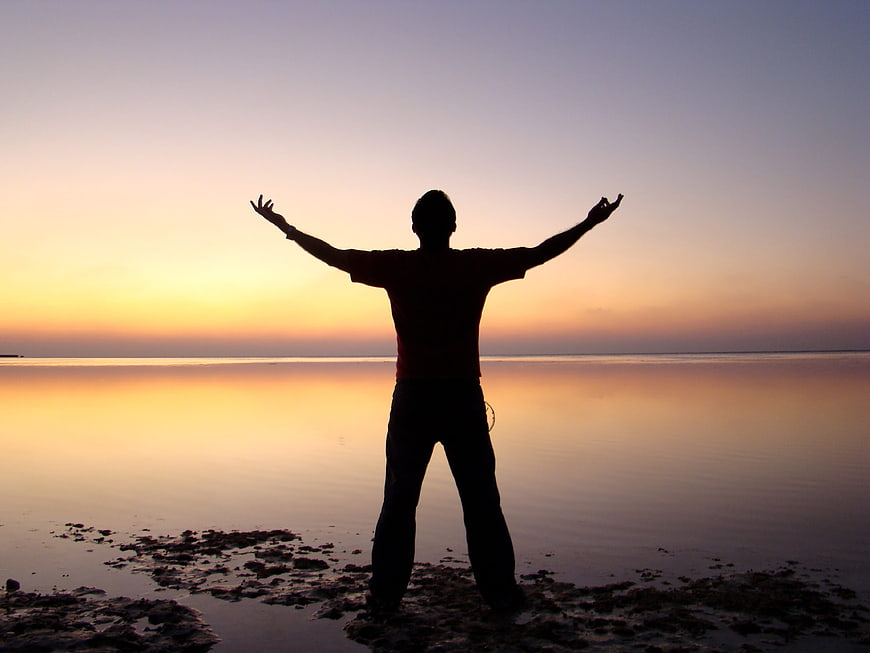 Silhouette of Man with Open Arms at Sunset on Beach