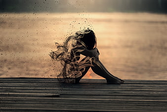 Woman dissolving into smoke on wooden pier at sunset