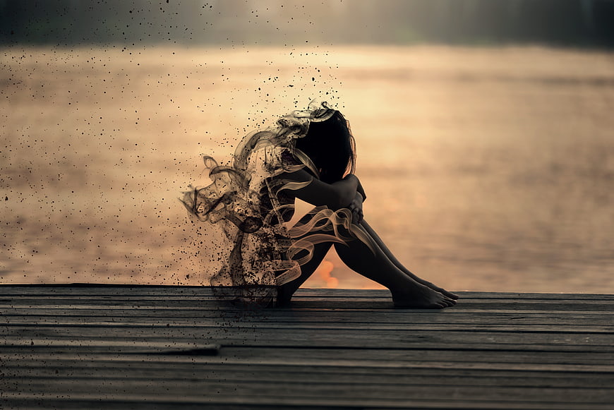 Woman dissolving into smoke on wooden pier at sunset