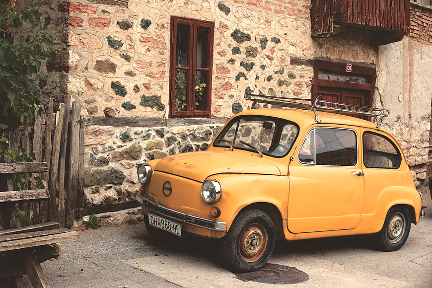 Vintage yellow car parked in front of rustic stone house