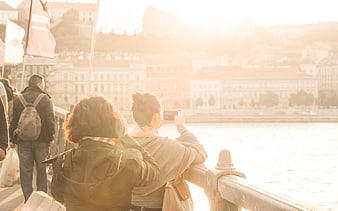 Woman taking photo of cityscape from bridge at sunset